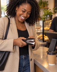 Woman laughing as she tries to squeeze an overstuffed fold wallet shut at a café counter