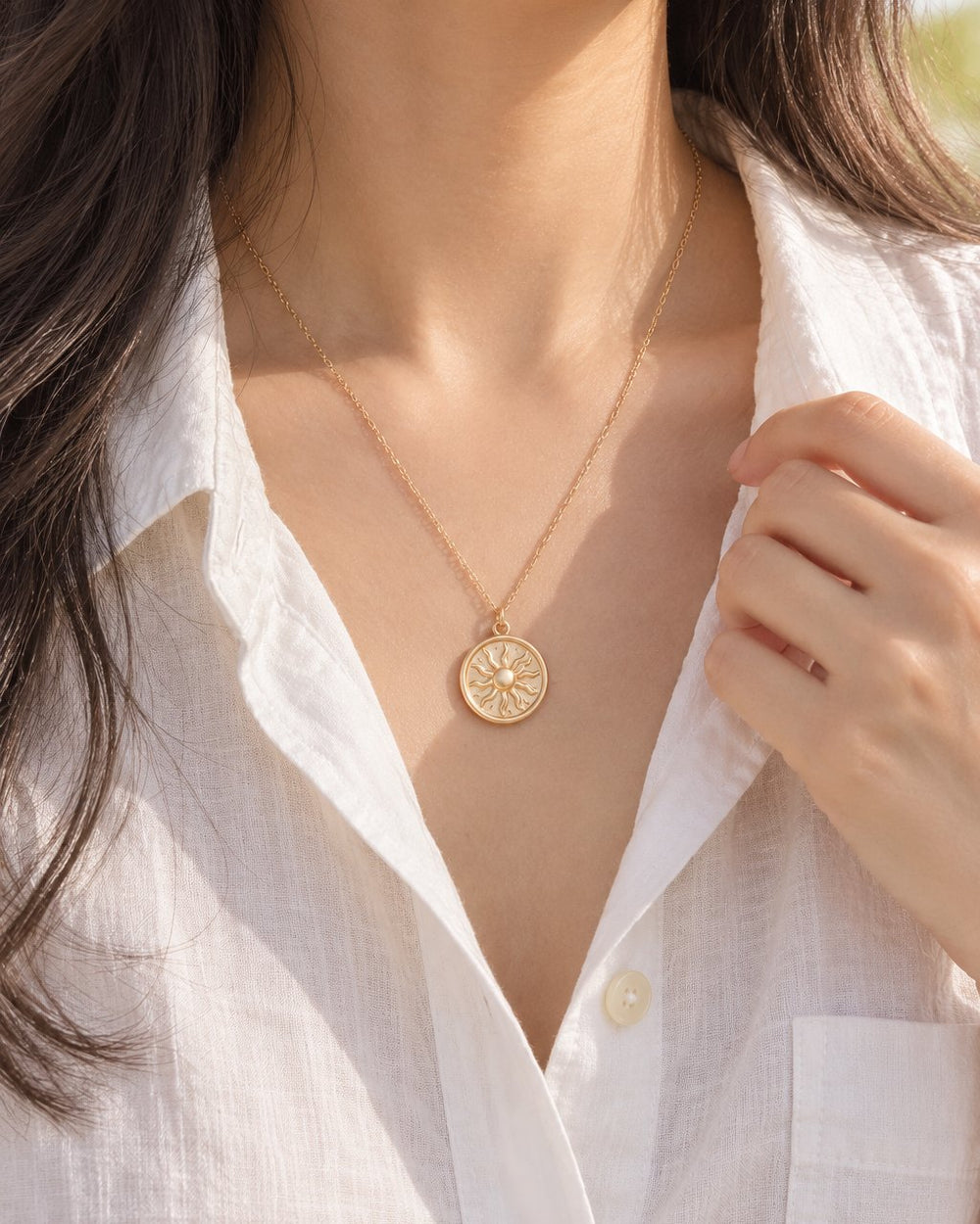 Woman in an open-collar white linen shirt wearing the sun coin just below her collarbone