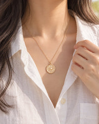 Woman in an open-collar white linen shirt wearing the sun coin just below her collarbone
