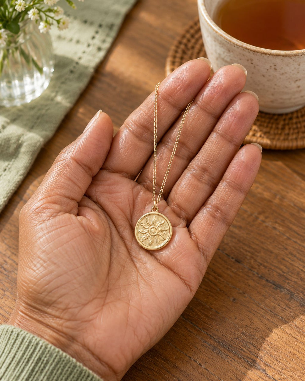 The 2 cm sun coin resting in a hand beside a cup of tea