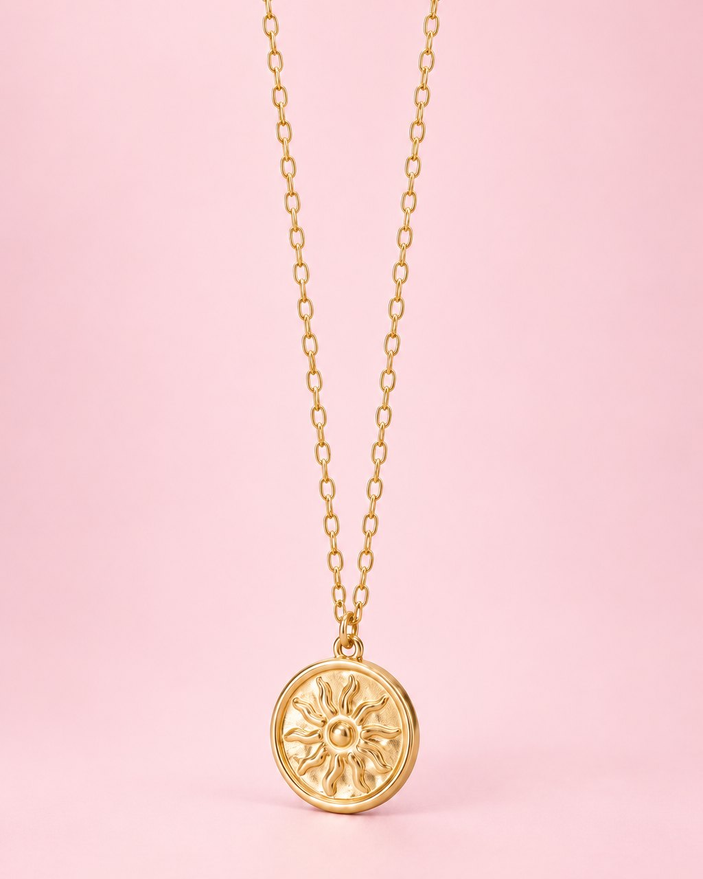 Gold-tone round coin pendant with an embossed sun on a fine chain