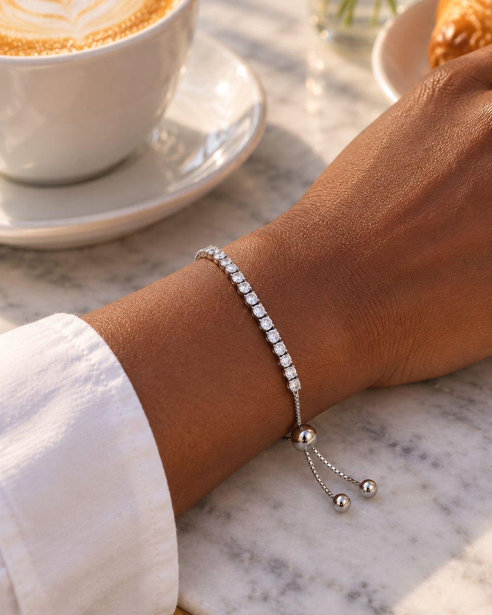 Wrist wearing the bracelet beside a cup of coffee on a marble café table