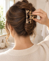 A woman presses the tortoise claw clip over a twist of brown hair at the back of her head