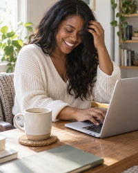 Woman laughing as she pushes loose hair out of her face while typing at a desk