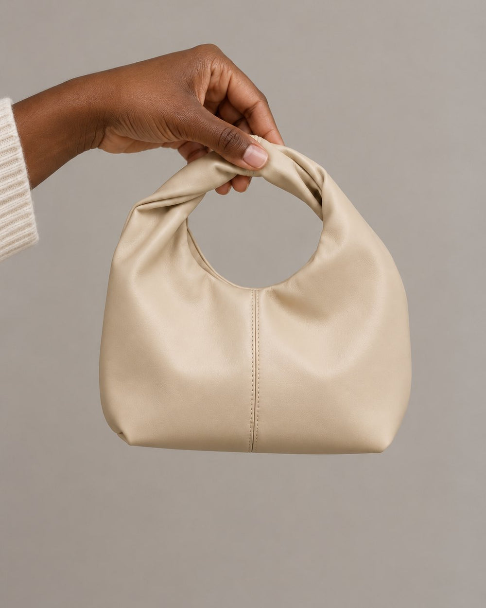 The mini bag held up by its handle in one hand, showing its compact size